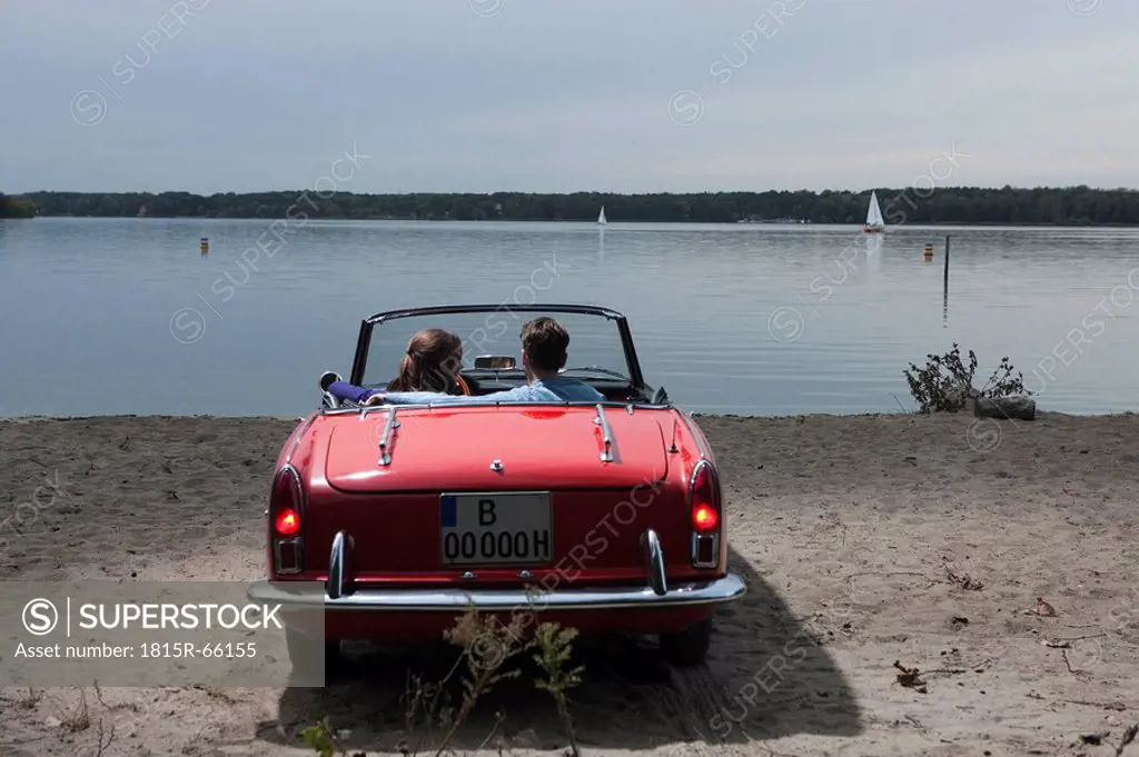 Germany, Berlin, Lake Wannsee, Young couple in cabriolet looking at lake, rear view