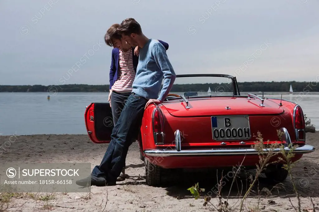 Germany, Berlin, Lake Wannsee, Young couple standing by cabriolet, looking down