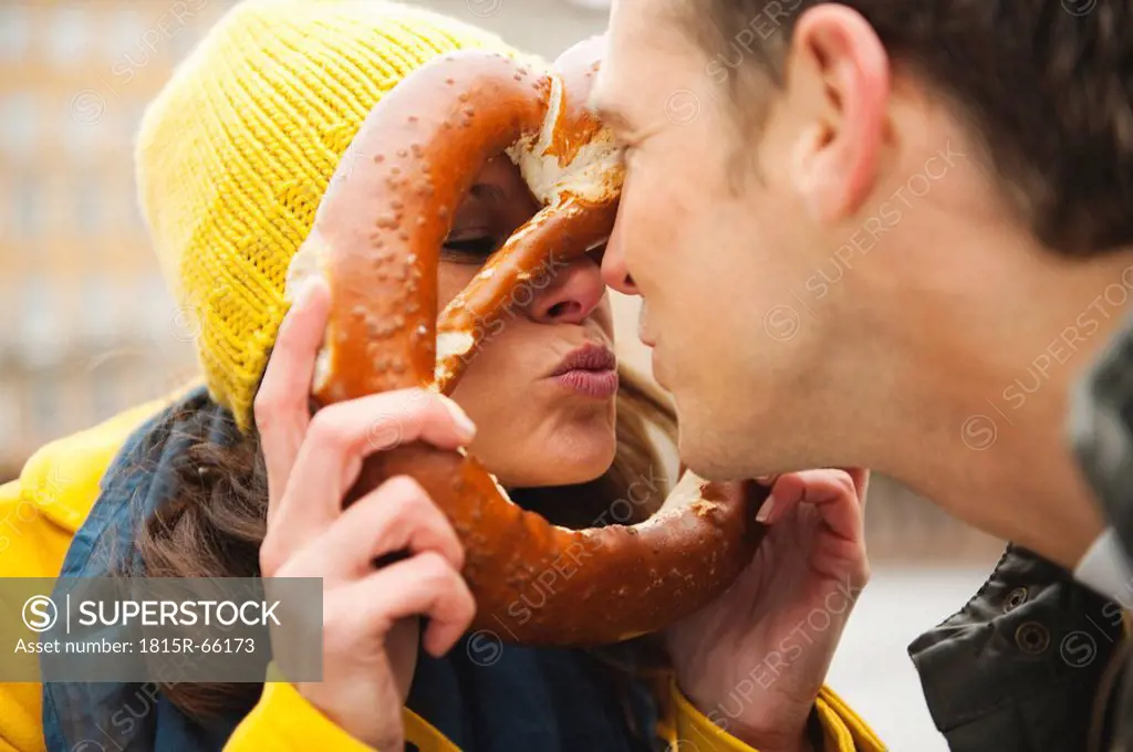 Germany, Bavaria, Munich, Couple, Woman holding pretzel in front of her face, puckering lips, portrait