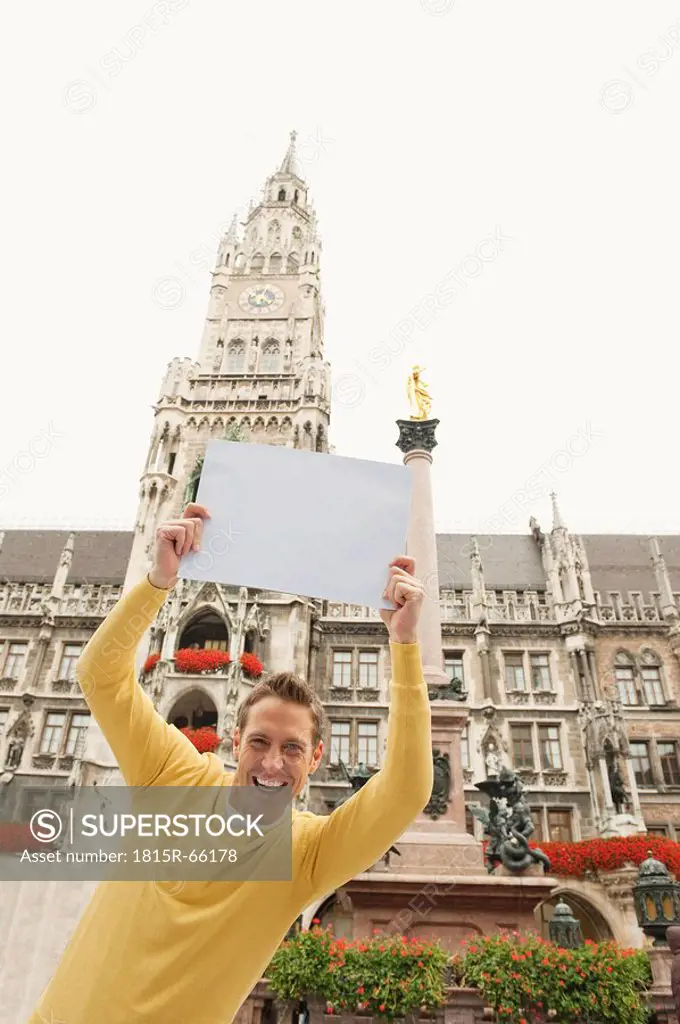 Germany, Bavaria, Munich, Marienplatz, Man keeping up blank card, smiling, portrait