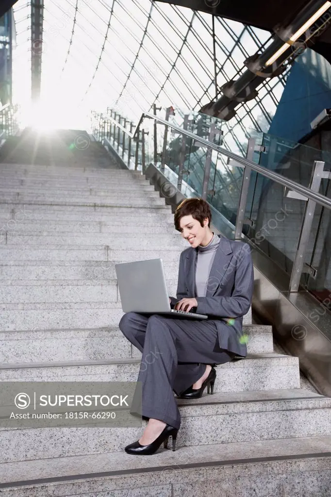 Germany, Bavaria, Munich, Business woman at subway station using laptop, sitting on staircase