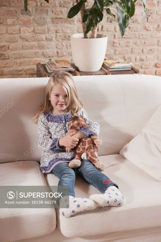Germany, Cologne, Girl 4_5 with a stuffed toy, sitting on sofa