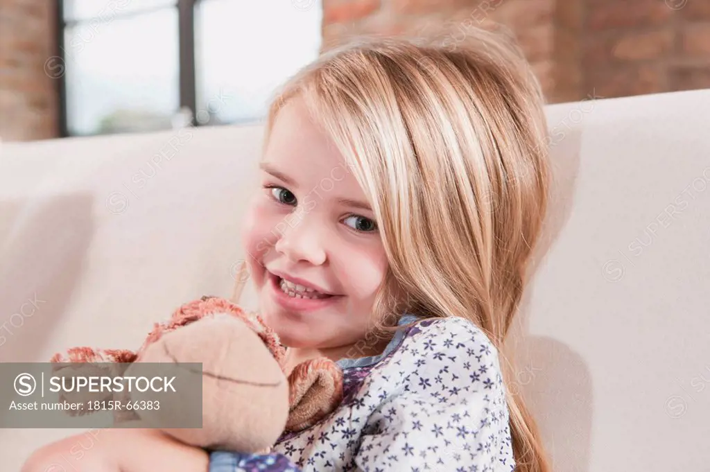 Germany, Cologne, Girl 4_5 with a stuffed toy, sitting on sofa