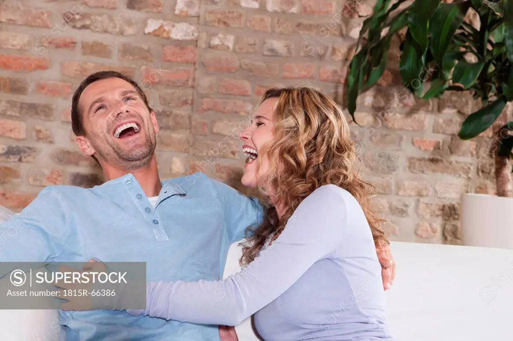 Germany, Cologne, Couple sitting on sofa, laughing, portrait