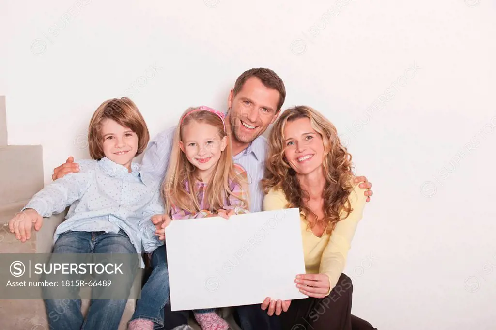 Germany, Cologne, Family sitting on steps of staircase using laptop, smiling, portrait