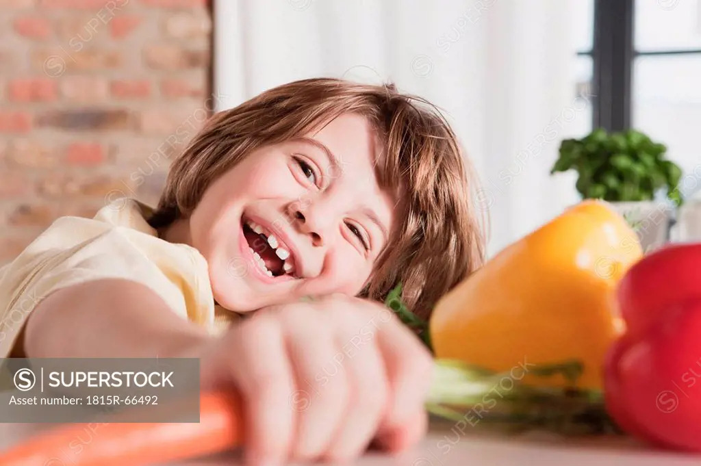 Germany, Cologne, Boy 6_7 in kitchen holding carrot, laughing, portrait, close_up