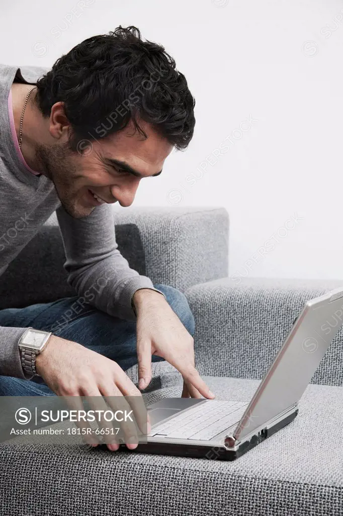 Man sitting on sofa using laptop, smiling