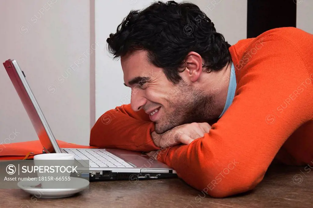 Man with coffee cup, smiling at laptop