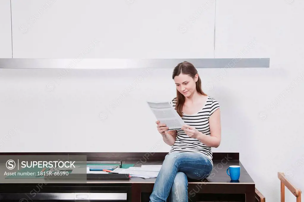 Woman sitting on desk reading document.