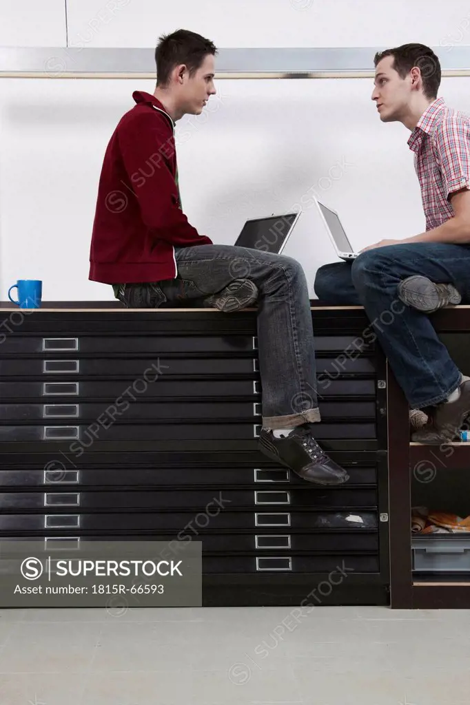 Men sitting face to face using laptop