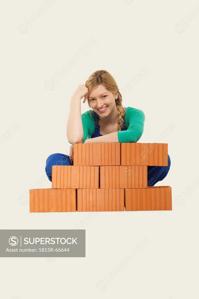 Woman sitting behind stack of bricks, smiling, portrait