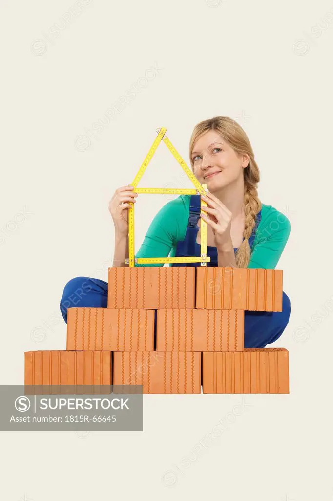 Woman holding tape measure sitting behind stack of bricks