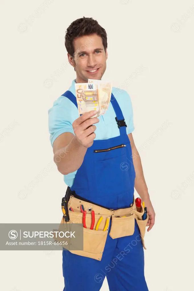 Man wearing tool belt holding currency, smiling, portrait