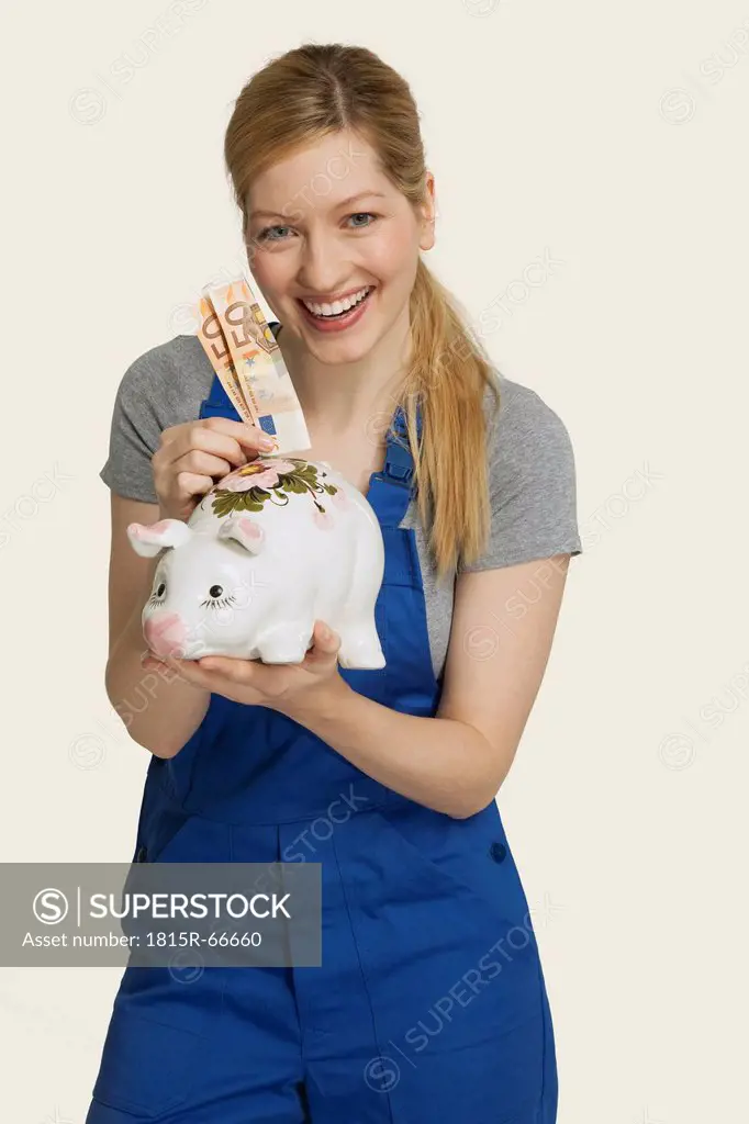 Woman in overall holding euro notes and piggy bank, smiling, portrait
