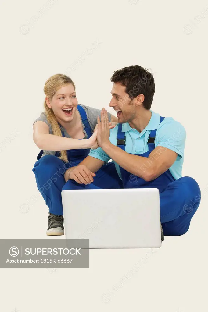 Man and woman in overall using laptop, giving high_five