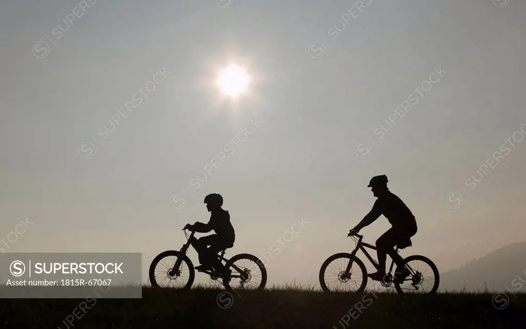 Father and son 10_11 riding mountain bikes, silhouette