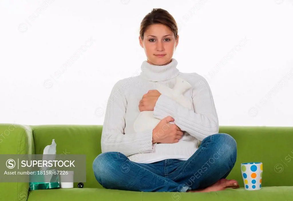 Young woman sitting on sofa, holding hot_water bottle