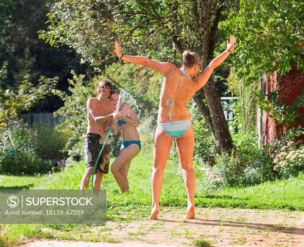 Austria, Salzburger Land, Teenagers 14_15 in garden having fun with hosepipe