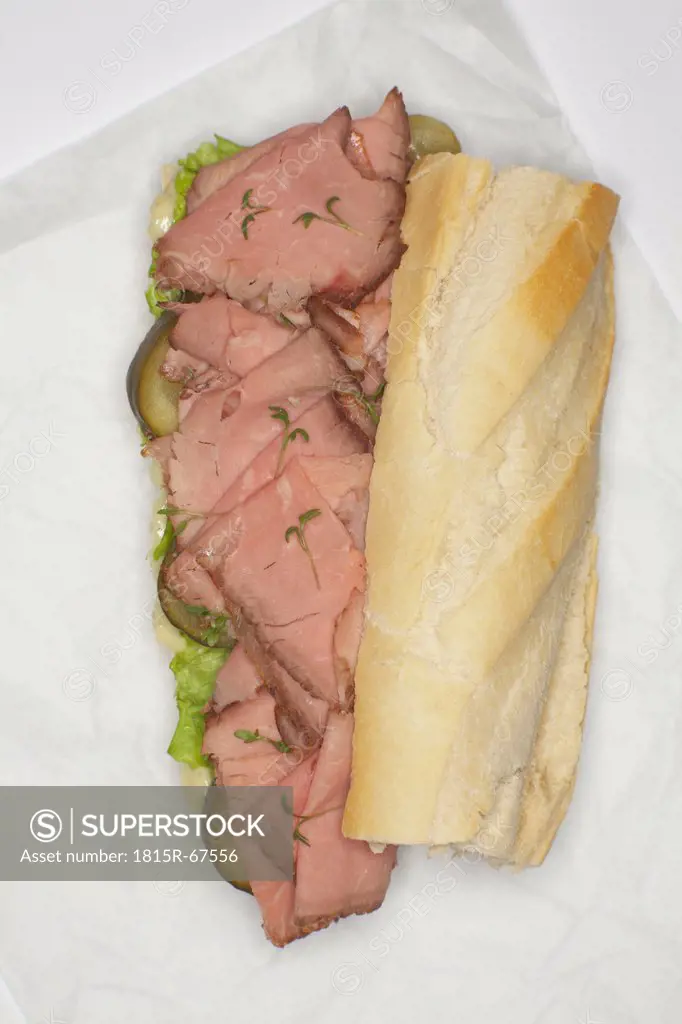 Baguette filled with slices of roast beef on wax paper.