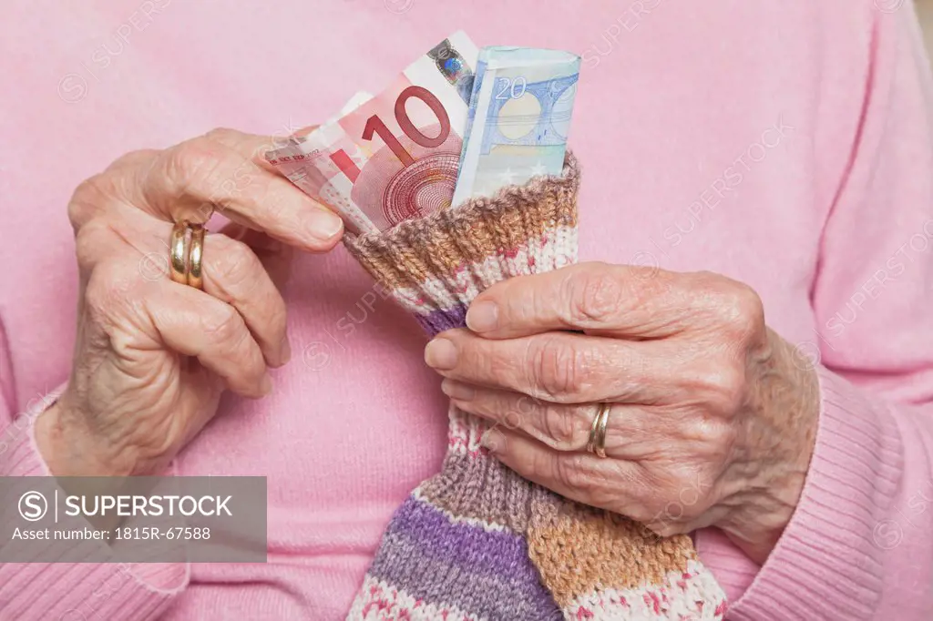 Germany, Senior woman counting money from money sock, mid section