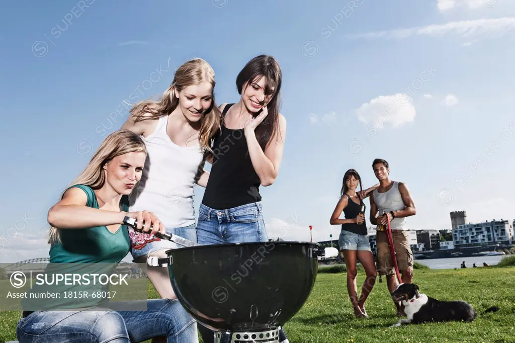 Germany, Cologne, Women barbecueing and friends in background with dog