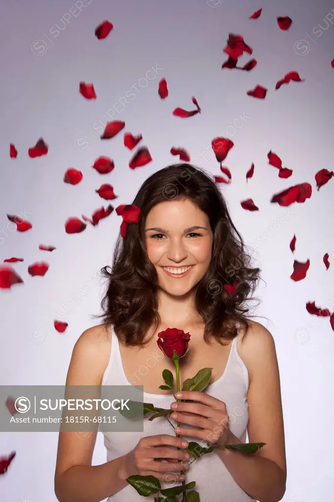 Young woman holding red rose, smiling, portrait