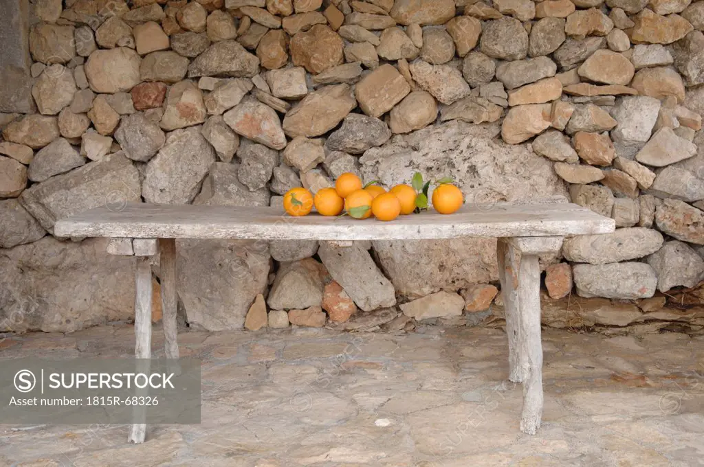 Oranges on bench against stonewall.