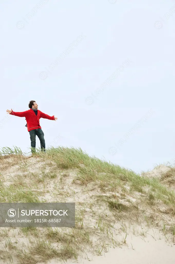 Germany, St Peter_Ording, North sea, Man standing on sand dunes with arms stretched