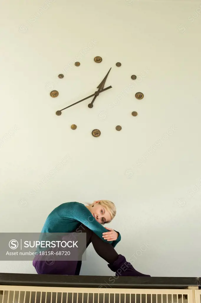 Germany, Leipzig, Young woman sitting against wall clock, portrait