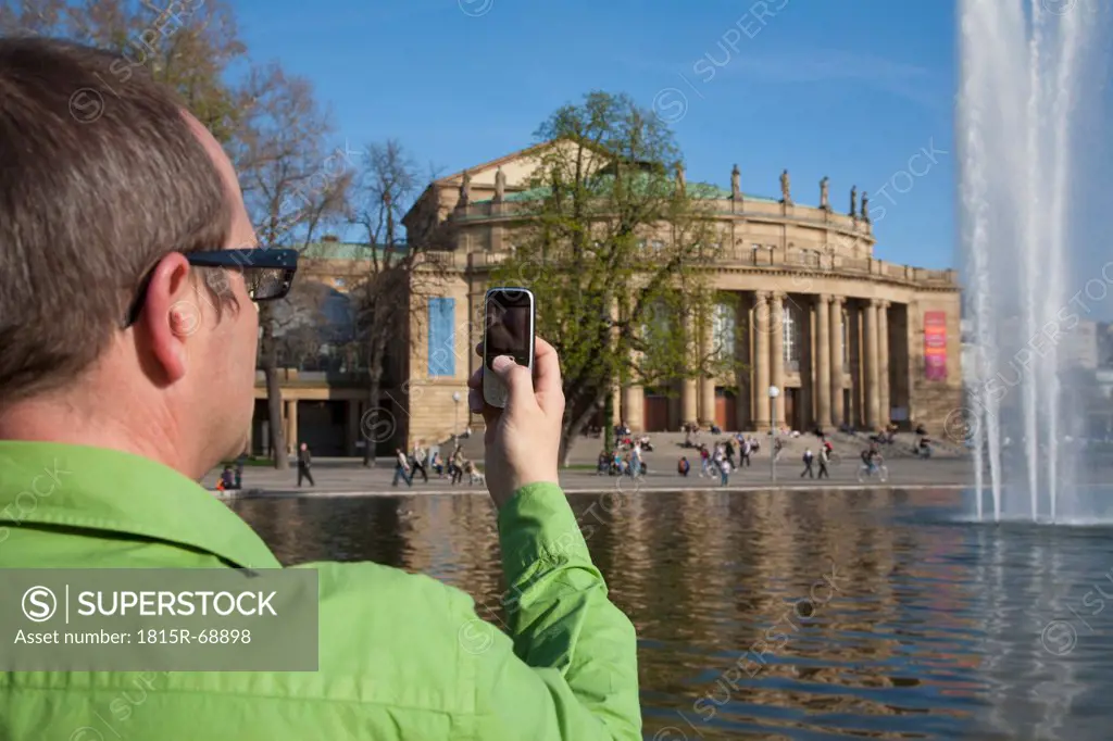 Germany, Stuttgart, Senior man capturing image of opera house from cell phone