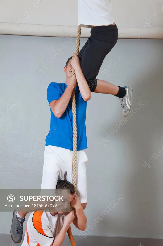Germany, Berlin, Young men and woman climbing rope in school gym