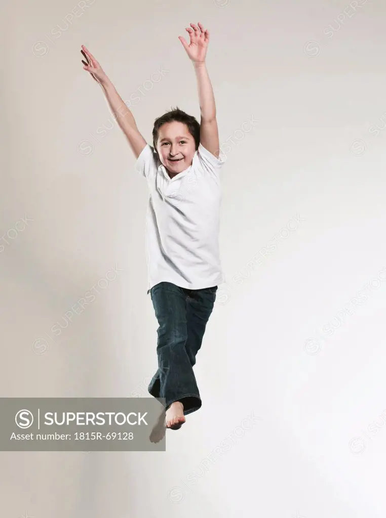 Boy 8_9 jumping with arms up, portrait, smiling