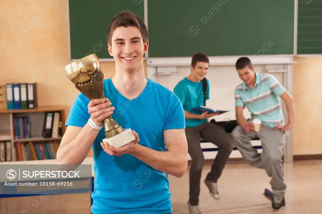 Germany, Emmering, Young man holding trophy with students in background