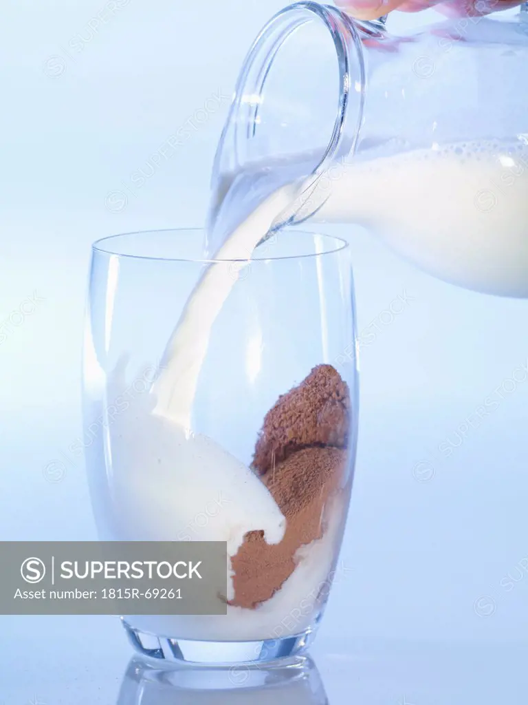Human hand pouring milk into glass of cocoa, close_up