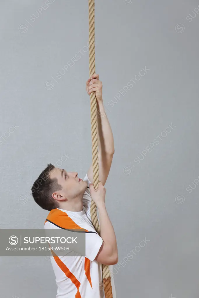 Germany, Berlin, Young man climbing rope in school gym
