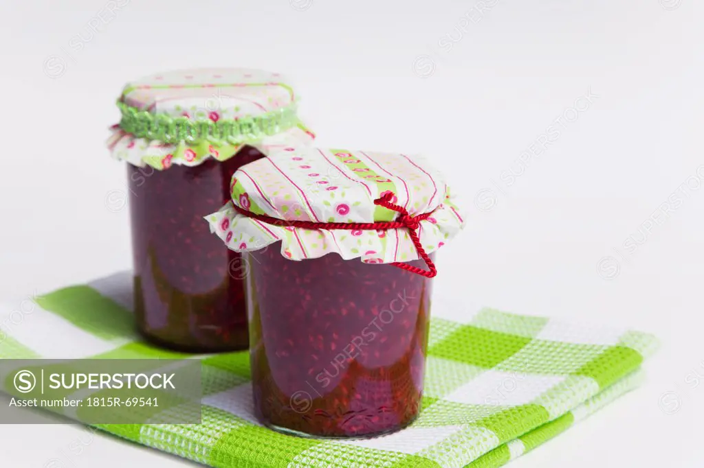 Raspberry jam bottle on tablecloth against white background