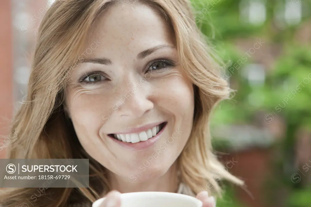 Germany, Woman holding coffee cup, portrait, smiling