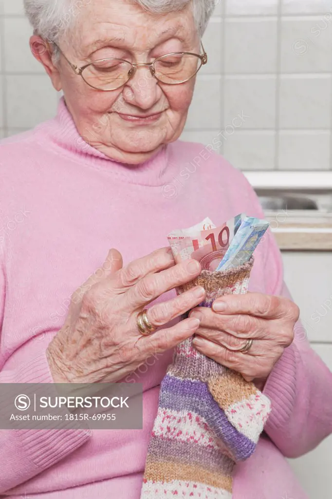 Germany, Senior woman counting money from money sock, smiling