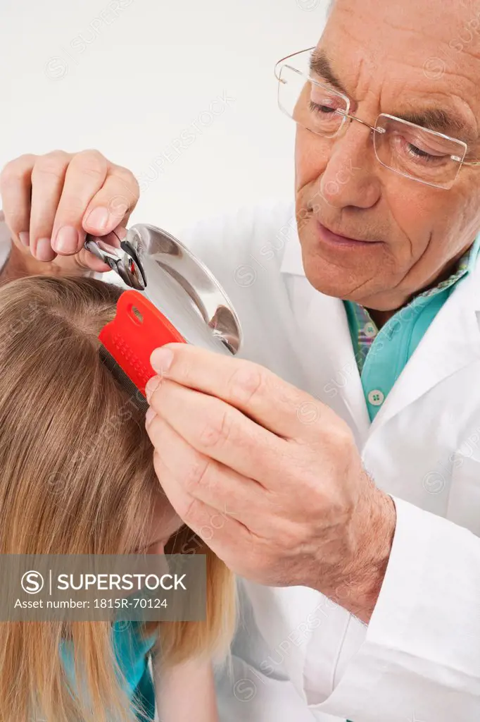 Germany, Munich, Doctor looking through magnifying glass into girl´s 8_9 hair