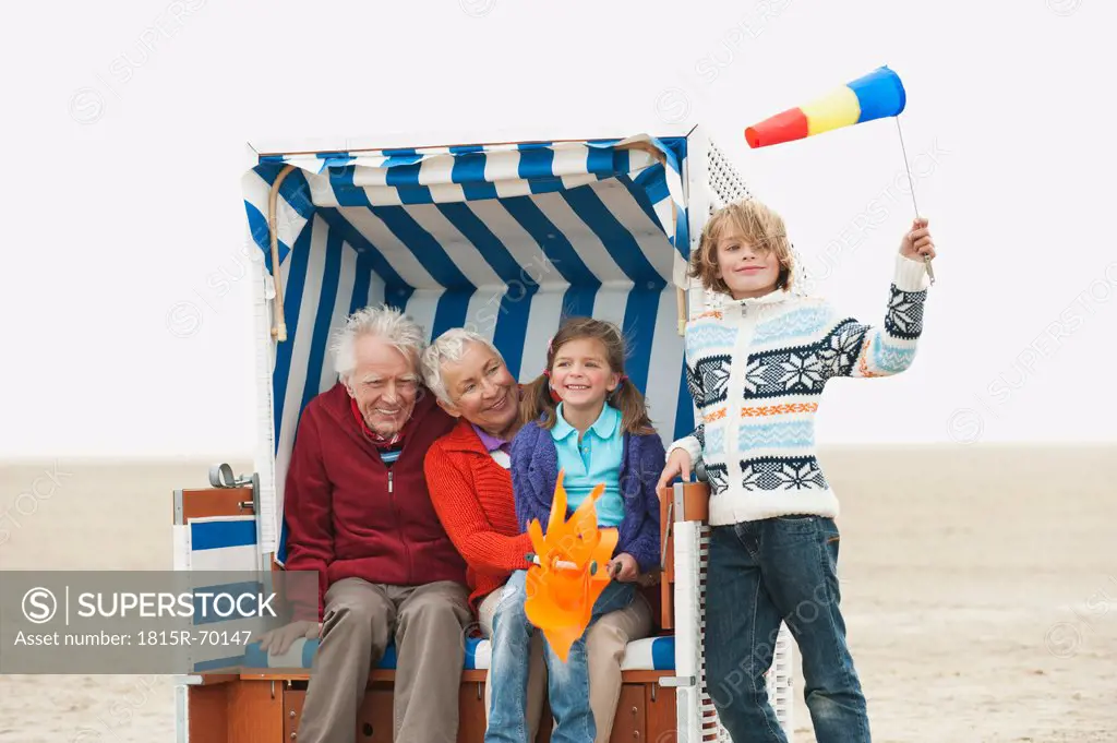Germany, St. Peter_Ording, North Sea, Grandparents with children 6_9 sitting on hooded beach chair