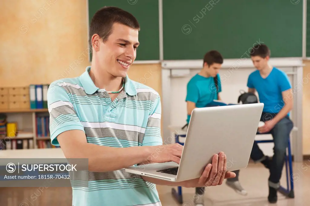 Germany, Emmering, Young man using laptop with students in background