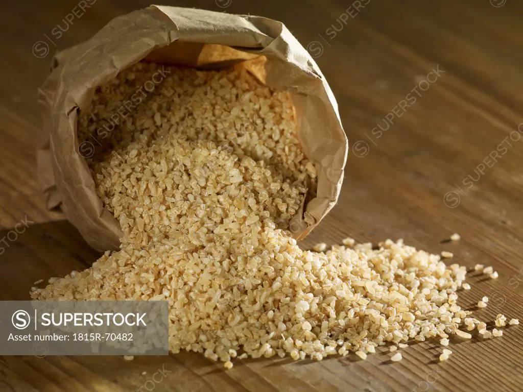Bulgur wheat grain spilling on wooden surface