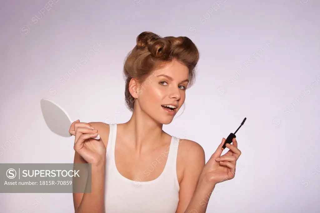 Young woman holding hand miiror and mascara brush, close_up
