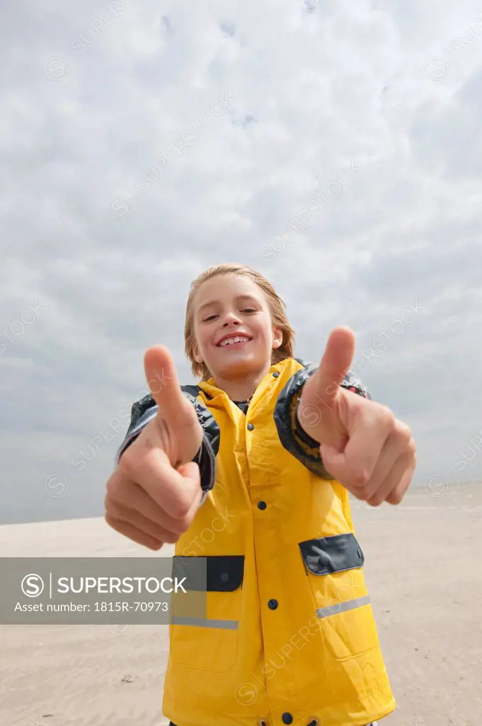 Germany, St.Peter_Ording, North Sea, Boy 8_9 in rain coat showing thumbs up sign on beach