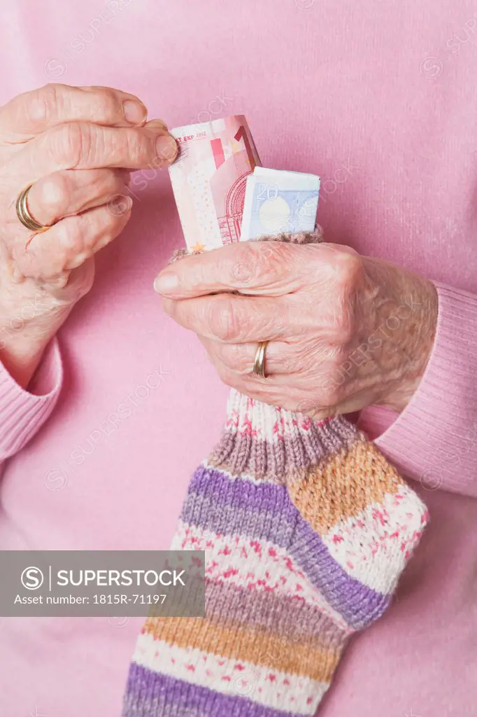 Germany, Senior woman counting money from money sock, mid section
