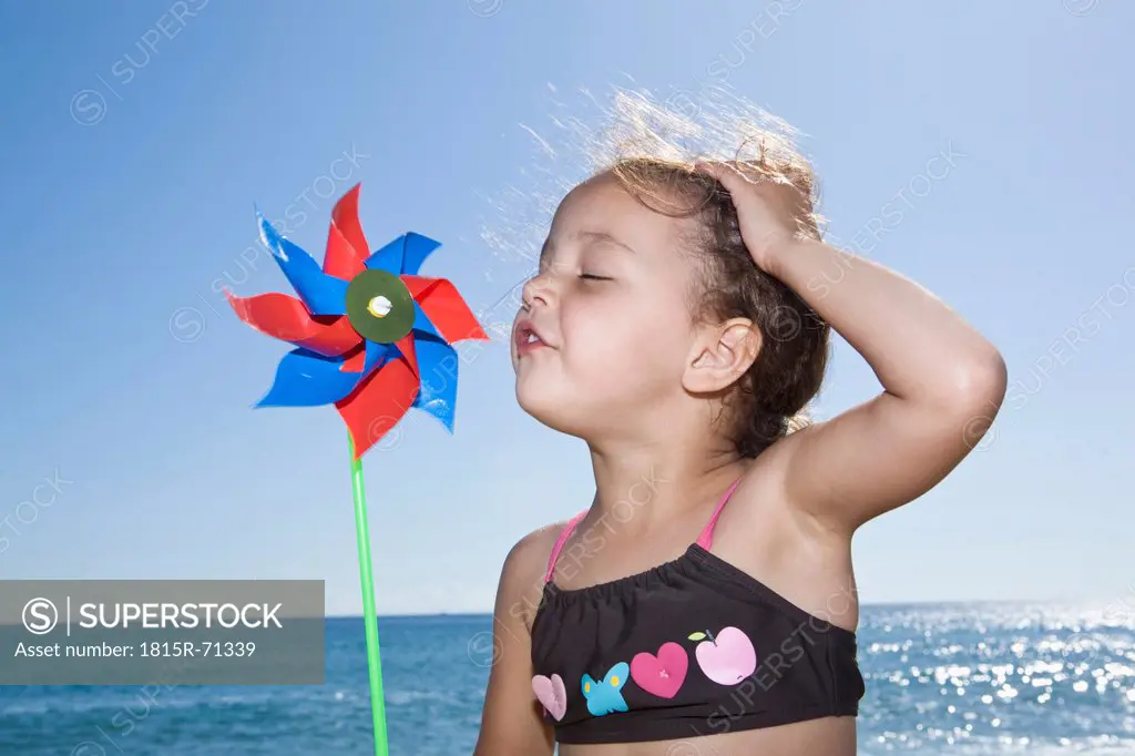 France, Corsica, Girl 2_3 blowing paper windmill on beach
