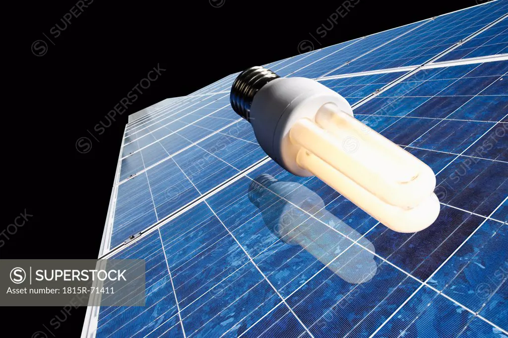 Energy saving lamp on solar panel against black background.