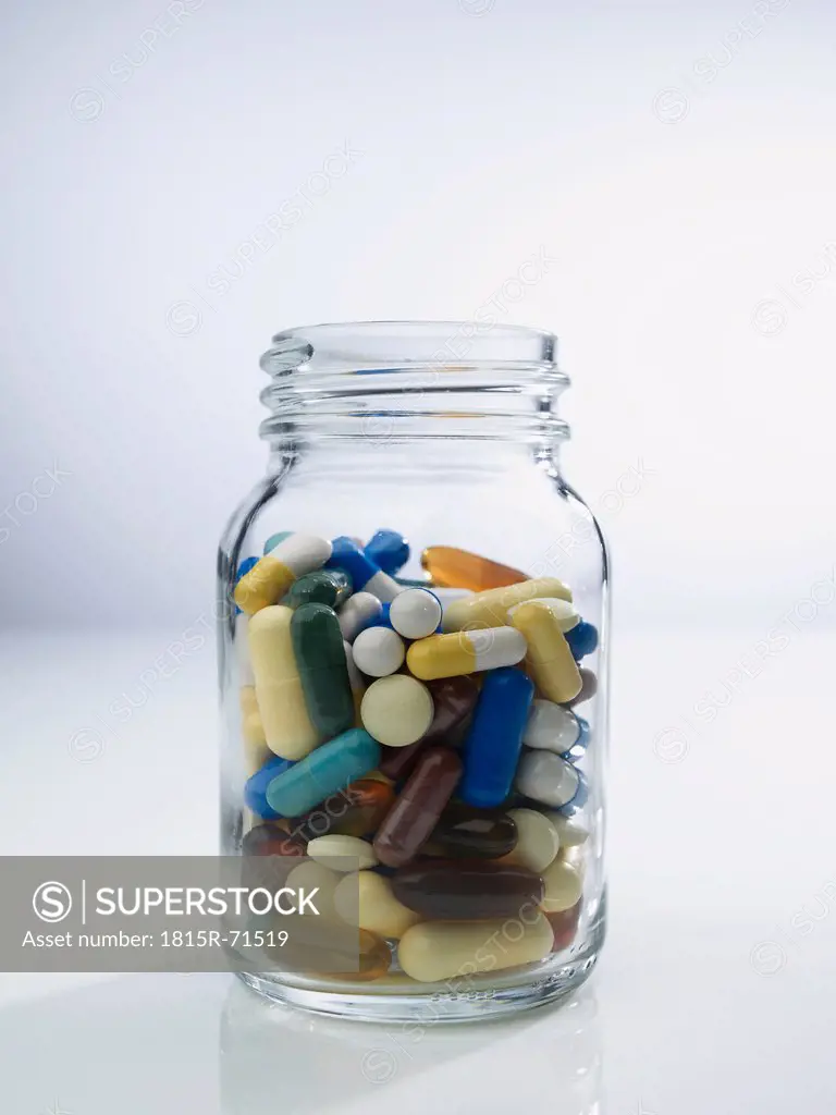 Glass jar full of pills on white background