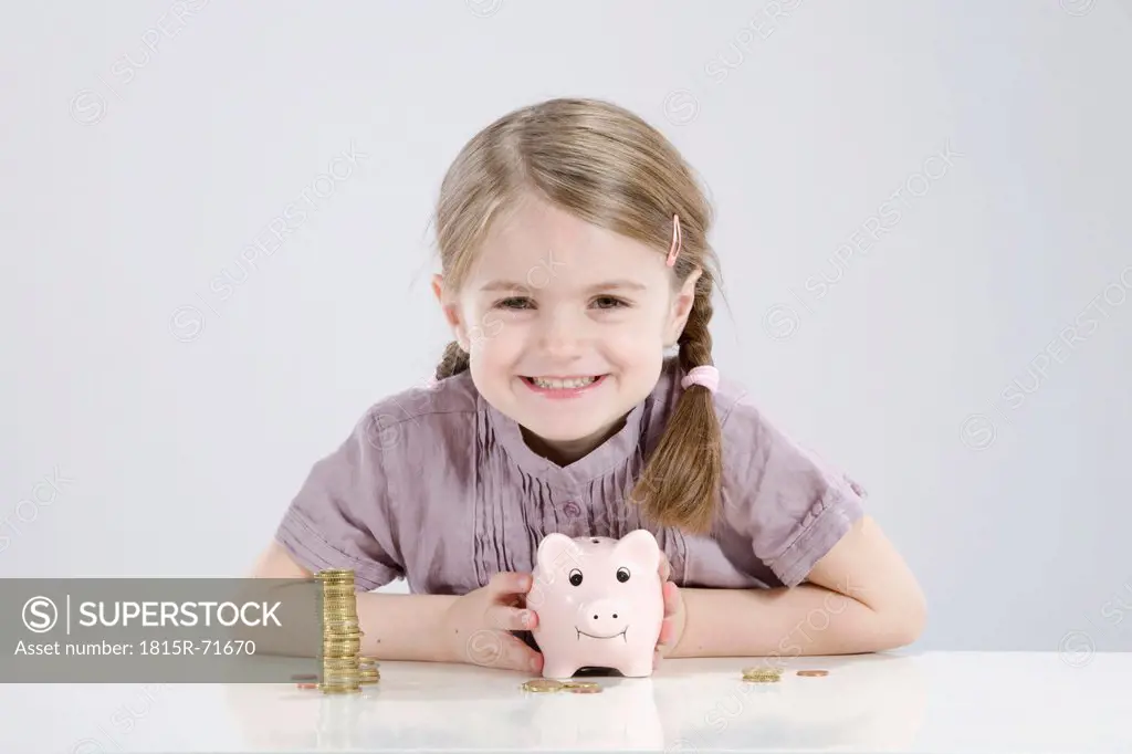 Girl 4_5 holding piggy bank and stack of coins, smiling, portrait