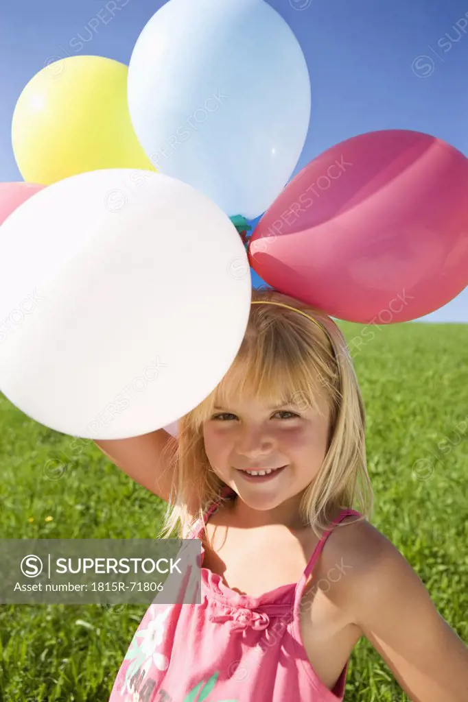 Austria, Mondsee, Girl 4_5 standing in meadow holding balloons, smiling, portrait